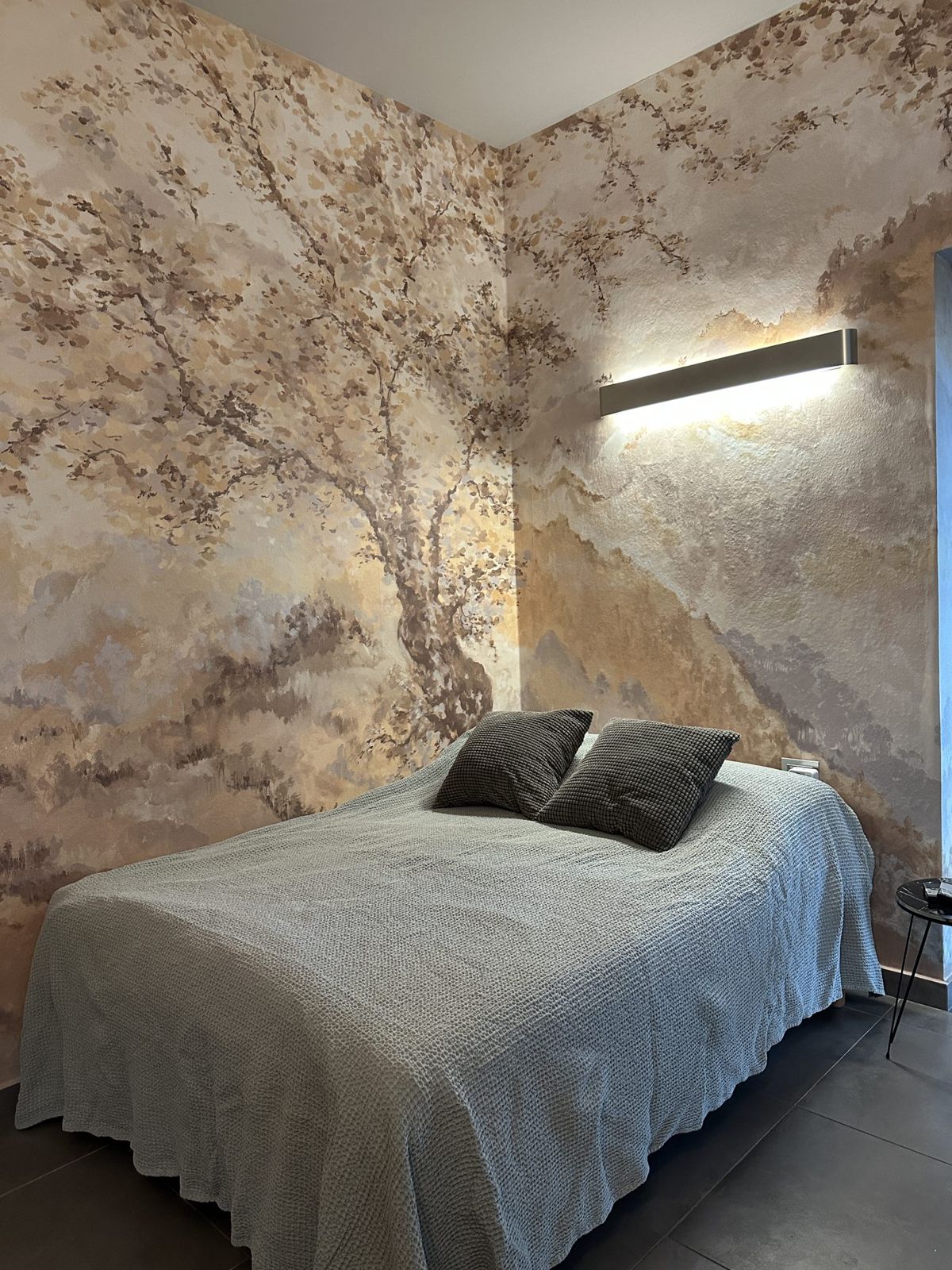Letto matrimoniale davanti al murale con albero in tonalità ocra